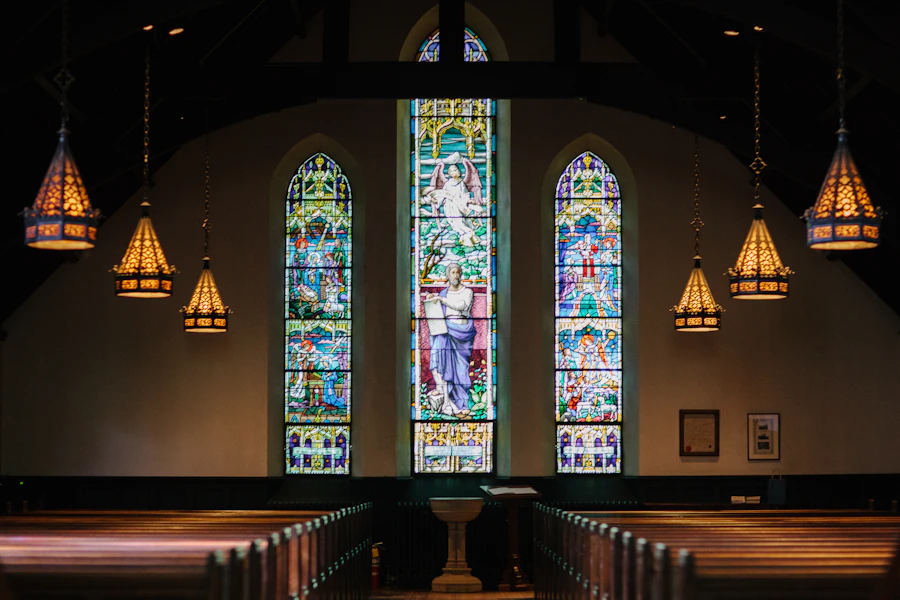 Wooden pews beneath three stained-glass windows in a church sanctuary